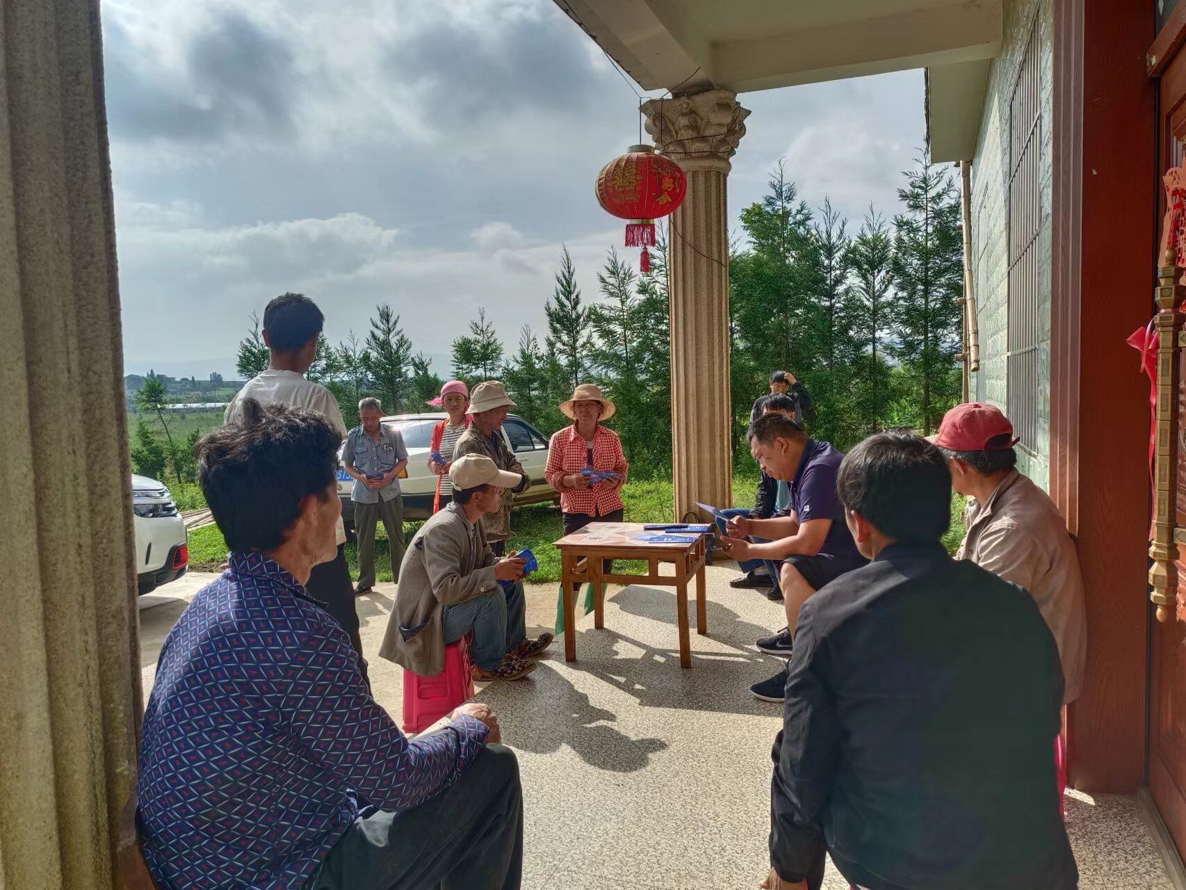 周强坐在木桌旁,一边低头看资料,一边与村民交流。 周强坐在木桌旁,一边低头看资料,一边与村民交流。