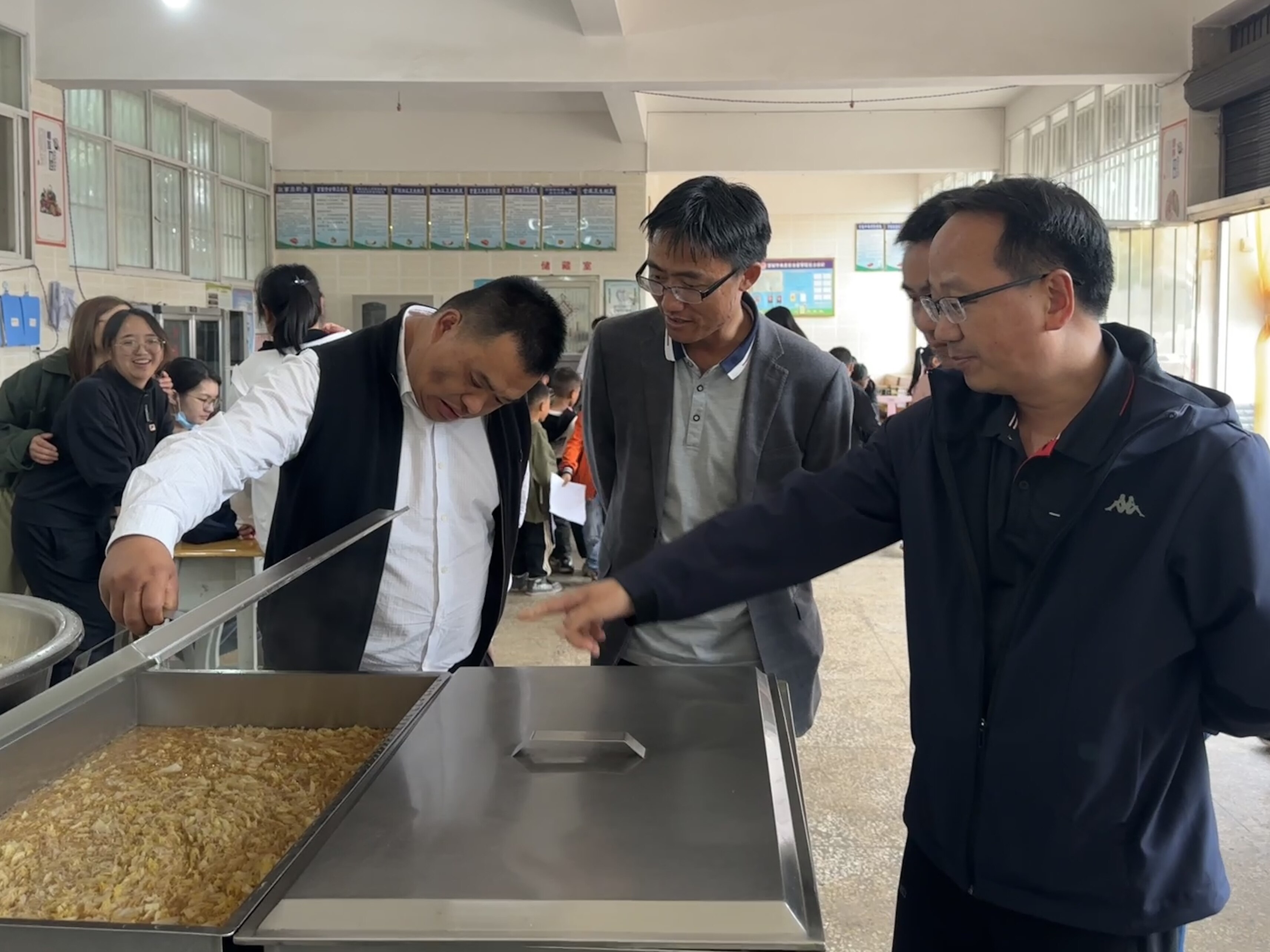 周强(左一)到小学食堂查看饭菜准备与供应情况。 周强(左一)到小学食堂查看饭菜准备与供应情况。